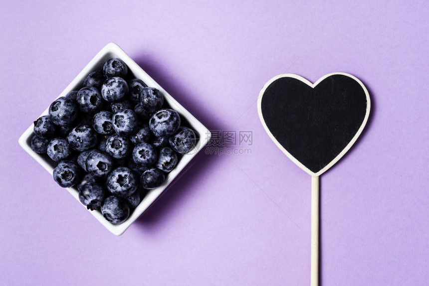 在紫色背景和心脏的罐子里的新鲜蓝莓图片