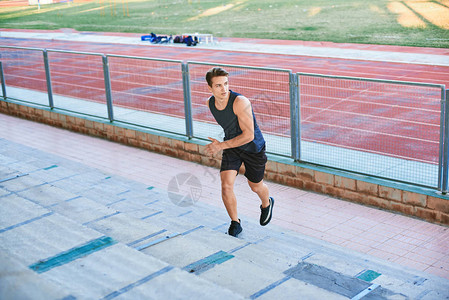 年轻的肌肉男在体育场上跑楼男运动员在体育场看台上奔跑健身运动图片