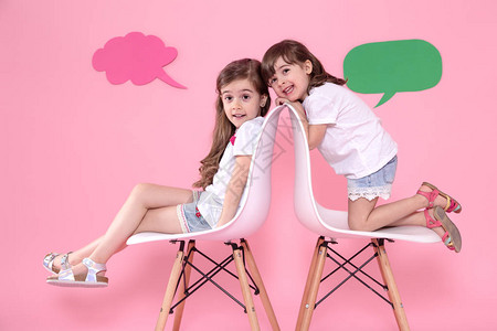 两位身着彩色粉红背景的小女孩坐在有演讲图标的椅子上交流与友谊背景图片