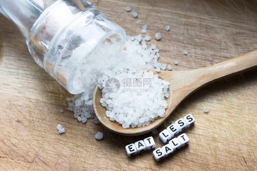 吃少点盐的讯息写在木勺子旁边充满了颗粒盐和摇晃器图片