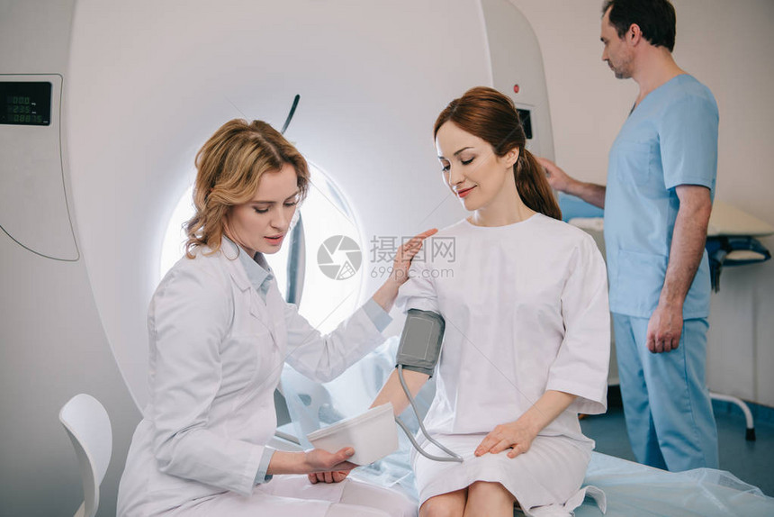 用计时测量病人血压和助理调整ct扫描仪的专心放射科医生图片