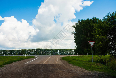 在柏油路前的土路十字路口让路的标景观与公路和树木蓝天白云愉快的驾图片