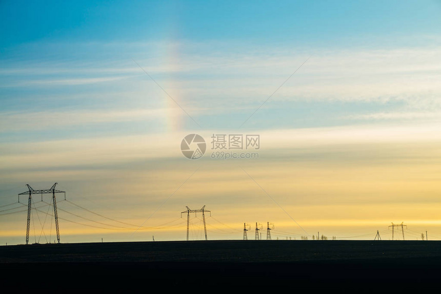 阳光明媚的天空背景上的电源线与彩虹特写具有复制空间的电线杆剪影地上高压电图片