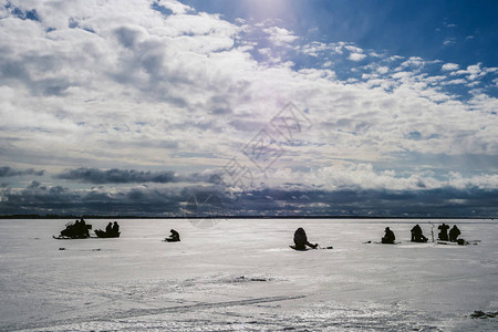 冬季渔民在蓝色云雾天空霜冻日下河冰上捕鱼和雪地图片