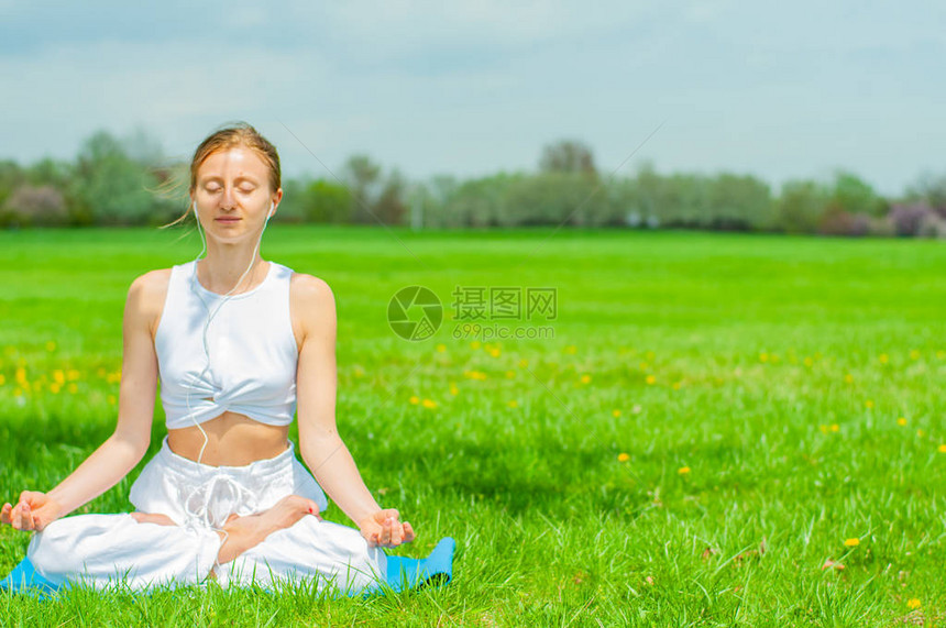 美丽的年轻女子正在练习瑜伽或冥想坐在公园草地上的莲花姿势做Padmasan图片