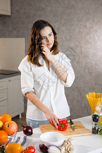 一位美丽的年轻女子在厨房里切菜和打电话素食主义者健康食图片