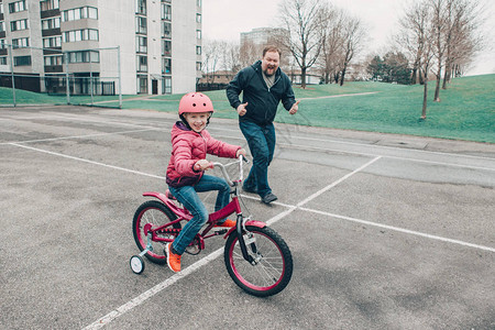 微笑兴奋的白种人父亲训练帮助女儿骑自行车图片