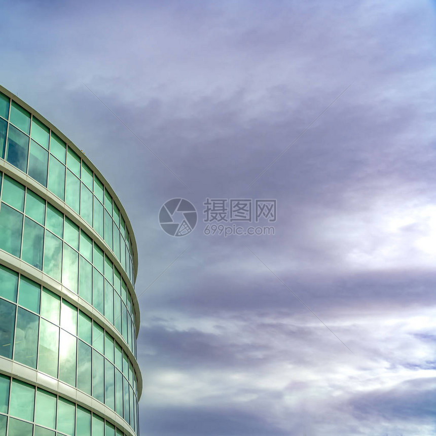 一座现代办公大楼的正方形外观有反射玻璃墙在楼上可以看到满是灰色云彩图片