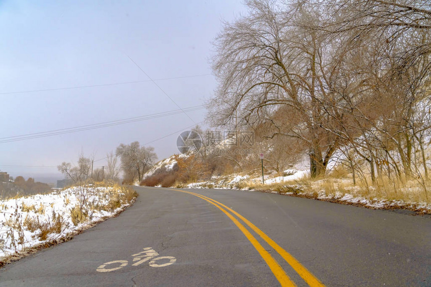 有自行车道标志的冬天路在表面上在盐湖城一座雪山上的道路反对天空弯曲的山路表面涂有白色的图片