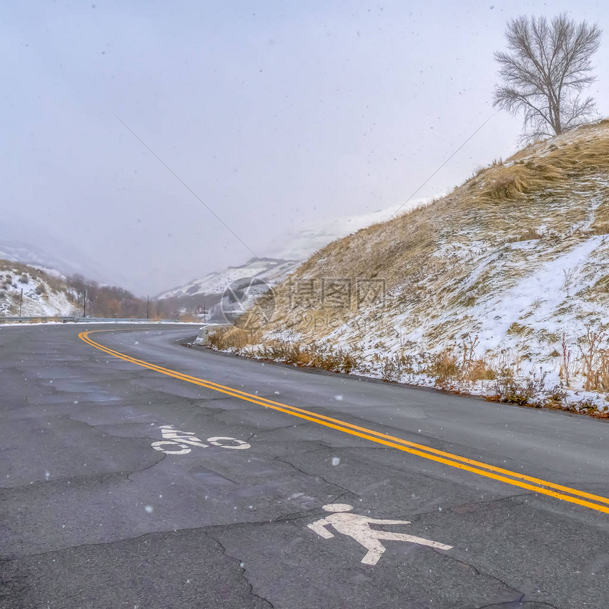 有行人和自行车道标志的方山路有行人和自行车道标志的道路绘在破裂的表面上这条路位于犹他州盐湖城一座积雪图片