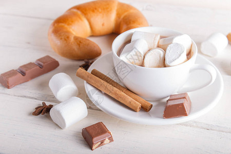 一杯热巧克力加棉花糖羊角面包和白木底的香料顶图片