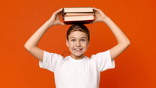 正面的学校男孩拿着一堆书在头顶上橙图片