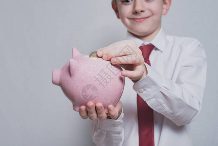笑男孩在粉红小猪银行放硬币商业概图片
