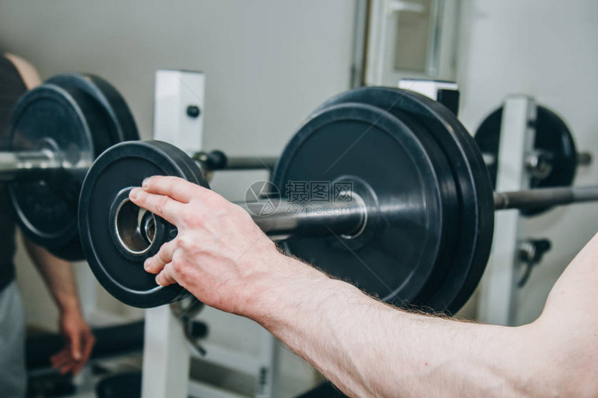 大手的运动员通过金属盘给训练中心的训练器械增加重量在健身房特图片