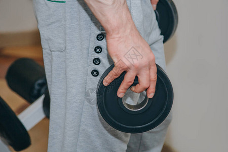 大手握着金属磁盘的运动员在训练中心健身房的训练工具在图片