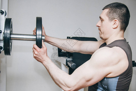 大手的运动员通过金属盘给训练中心的训练器械增加重量在健身房特图片