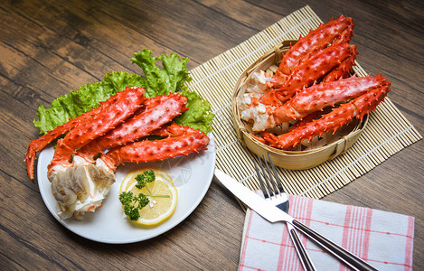 阿拉斯加国王螃蟹腿在白盘上煮熟了柠檬面生菜和竹船木制背景红蟹北图片