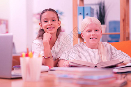 两个快乐的笑脸孩子坐在书和铅笔杯后面的书桌前图片