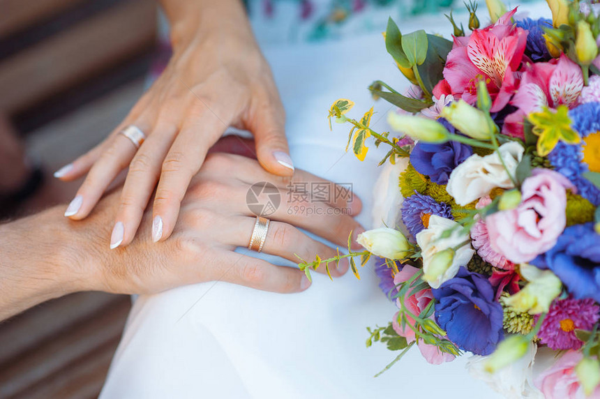 新娘和新郎的手指上戴着戒指在婚礼花束的背图片