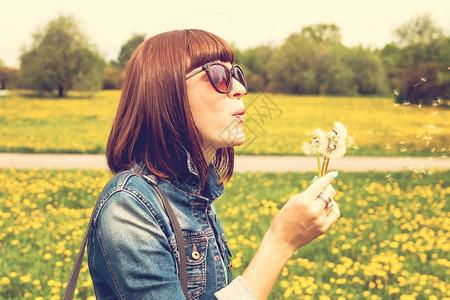 美丽的女孩在夏日公园吹花朵图片