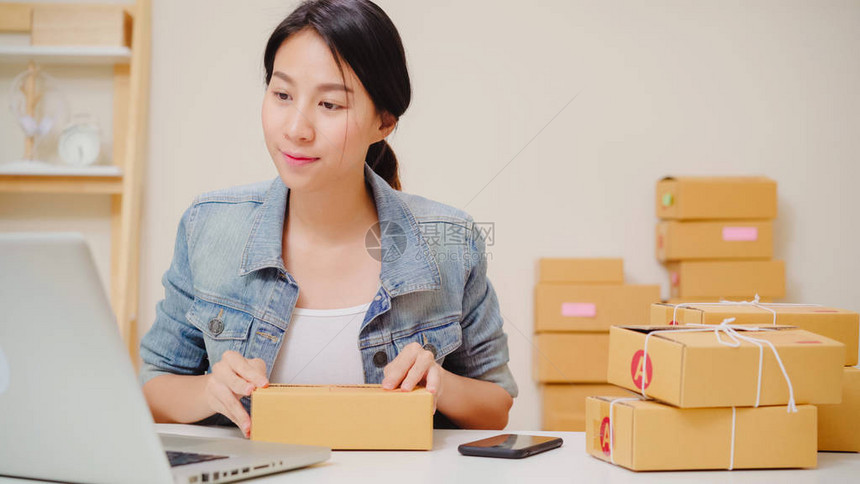 美丽聪明的亚洲年轻企业家女商人拥有SME在线检查库存产品并将包装放在家工作的盒子上家庭办公室概图片