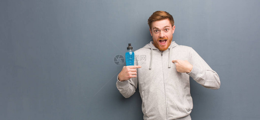 年轻红头发健身员惊讶地感到成功和繁荣他正在饮用能量饮料图片