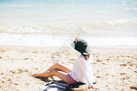 戴着帽子的时尚髦女孩坐在海滩上图片