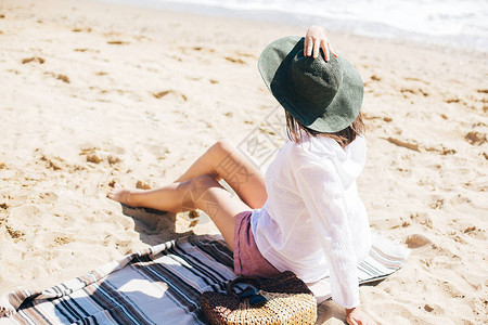 戴着帽子的时尚髦女孩坐在沙滩上图片