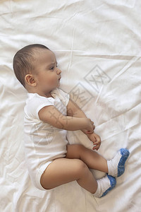 68个月大的男婴顽皮地躺在床上穿着白色紧身衣裤的迷人67个月小婴儿白色床上用品的男背景