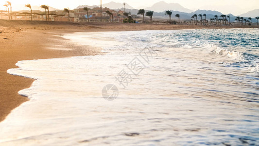 美丽蓝色海洋波浪在沙海滨与惊人的日落之间滚动图片