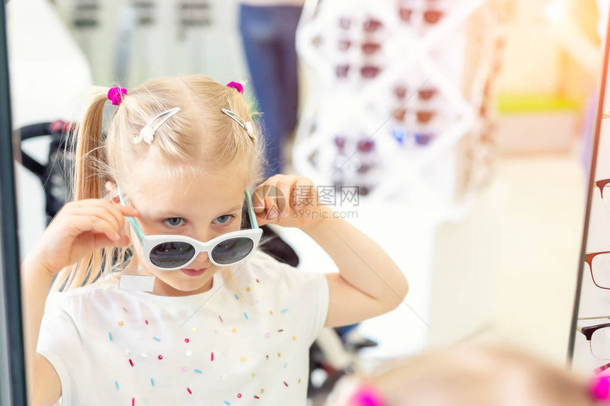 可爱的年轻白种人金发女孩在光学眼镜店的镜子前试戴和选择太阳镜可爱的女学生在商店里戴太阳紫外线防护图片