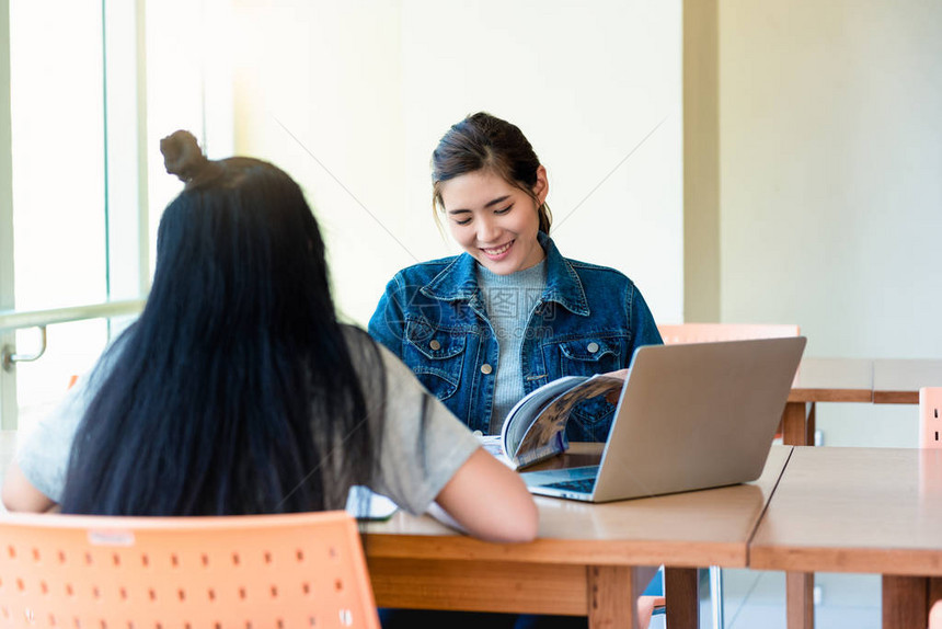 亚洲女学生在学院大学图书馆的木桌上用笔记本电脑打开阅读杂图片