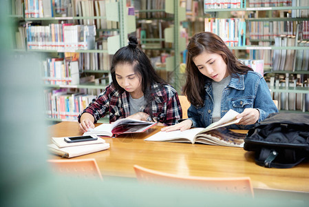 两名亚洲女学生在图书室打开阅读教科书在国际学院大学的图片