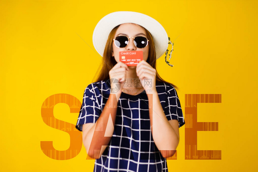 戴着太阳镜的亚洲年轻女肖像的模糊图像手持和亲吻信用卡与销售文本双重曝光购物年中销售概念隔离图片