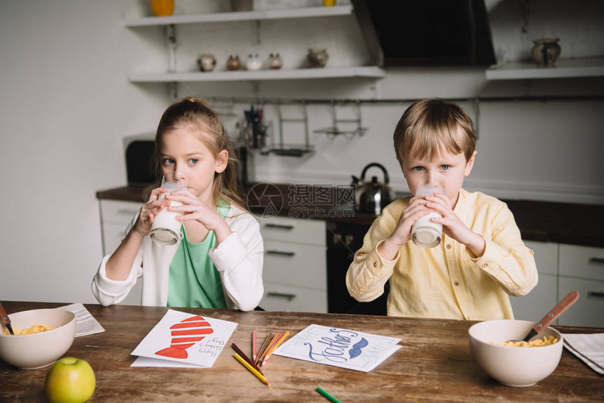 可爱的小孩一边喝牛奶一边坐在厨房桌边吃饭图片