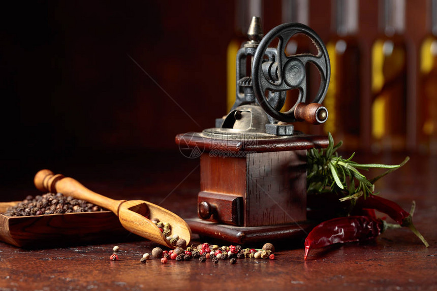 老式胡椒磨用各种辣椒和香料棕色背景上有炊具橄榄油瓶香料和迷迭图片