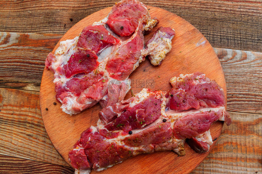 在乡村餐桌上的木制切菜板上加香料的新鲜生猪肉顶视图图片