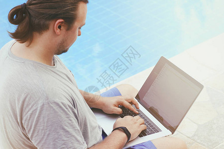 有笔记本电脑的年轻人坐在泳池附近户外工作场所自由概念网上购物休图片