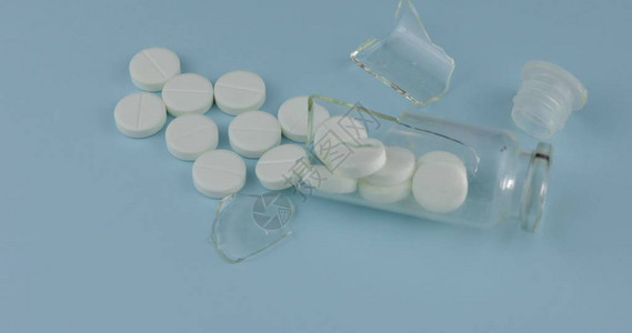 破碎玻璃罐许多白圆丸和蓝底药物药品图片