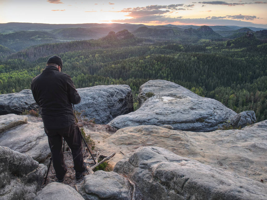 摄影师在三脚架上检查相机的显示男人呆在悬崖上拍照和朋友聊天秋天美丽的朦胧景观朦胧的图片