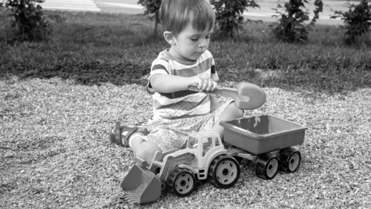 3岁小孩男坐在公园的沙箱里玩具卡车挖土机和拖车图片