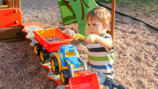 快乐的微笑男孩在带拖车的玩具卡车里倒沙子的画像孩子们在公园的操场图片