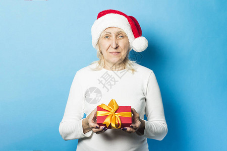 圣诞老人帽子的老妇人拿着礼物反对蓝色背景庆祝圣诞节新年寒假购图片