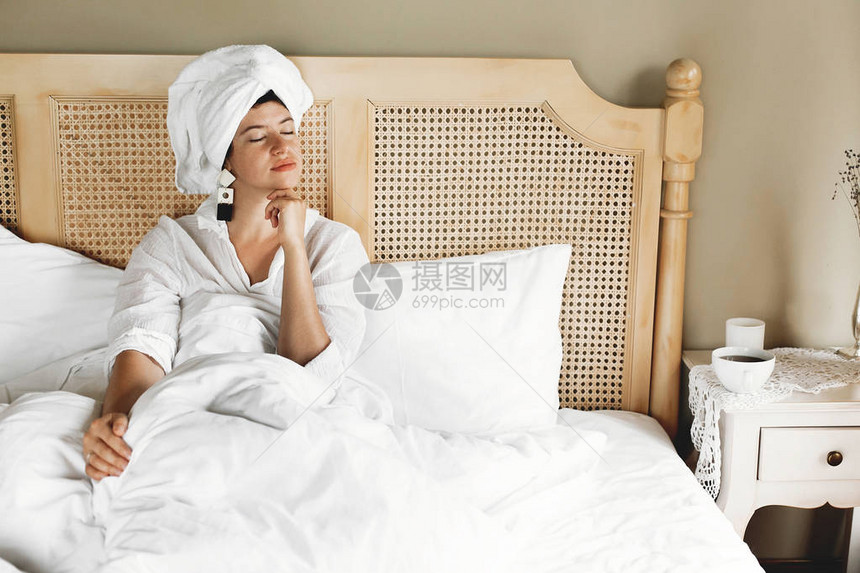时髦的年轻女子在旅馆房间或家庭卧室的床上放松图片