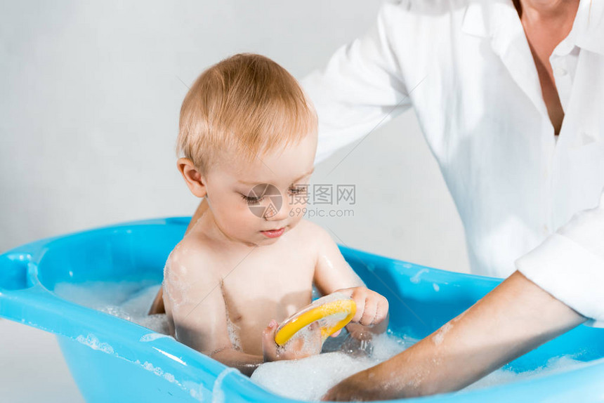 在蓝色婴儿浴缸里母亲洗可爱的小孩图片