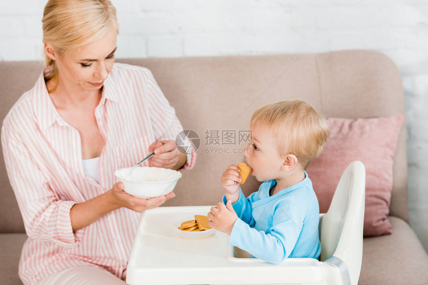 金发母亲拿着勺子和婴儿食物在可爱的小孩儿子旁边图片
