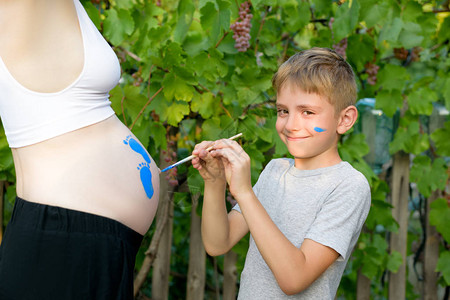 快乐的小男孩在怀孕妈宝足迹的肚子上画图片