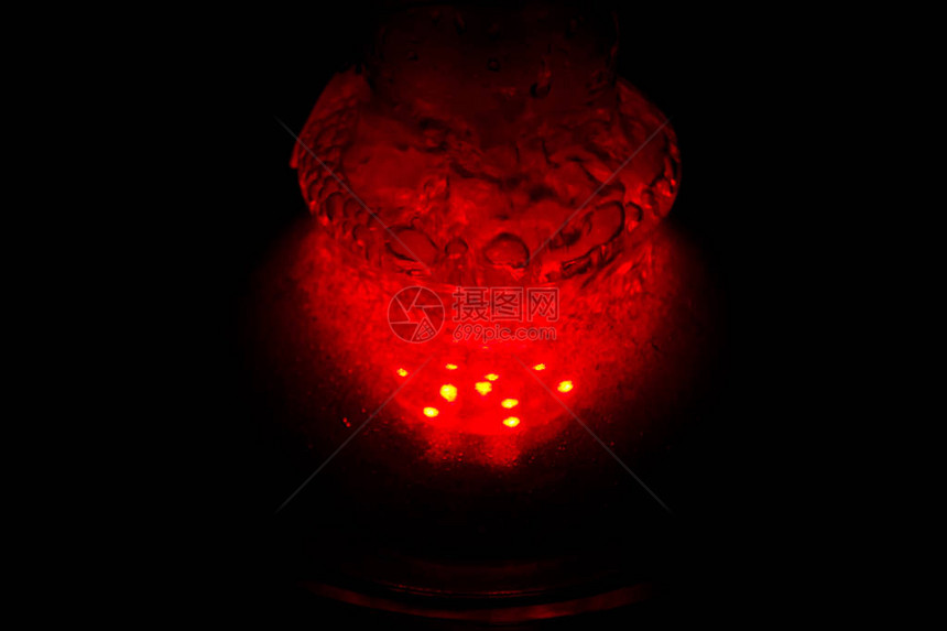 一个装满冒泡的水和烟雾的玻璃水烟壶在黑暗中发出红色的光芒图片