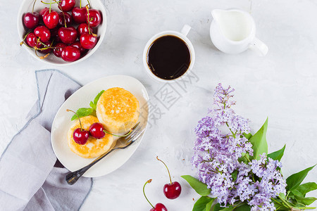 夏季早餐干酪煎饼配浆果樱桃一杯黑咖啡牛奶和白桌背景上的樱图片