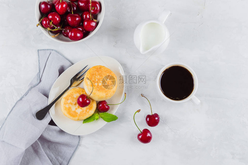 夏季早餐干酪煎饼配浆果樱桃一杯黑咖啡牛奶和白桌背景上的樱图片